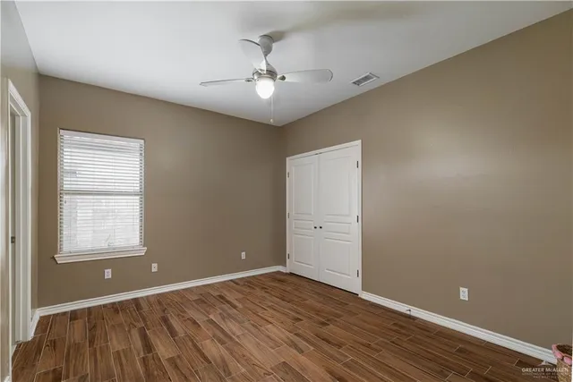 an empty room with wooden floor chandelier fan and windows