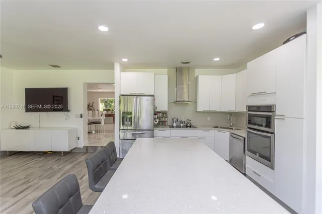 a kitchen with stainless steel appliances kitchen island granite countertop a refrigerator a stove top oven and a dining table with wooden floor