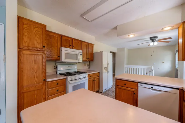 a kitchen with stainless steel appliances granite countertop a stove top oven a sink dishwasher a refrigerator and a dining table with wooden floor