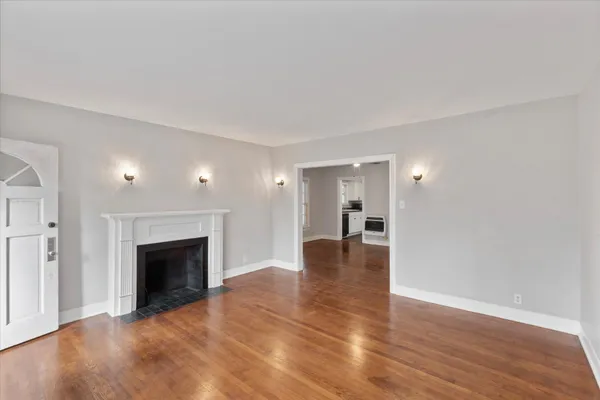 a view of an empty room with wooden floor fireplace and a window