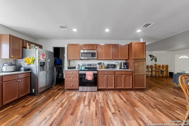 a kitchen with stainless steel appliances wooden floors a refrigerator and a stove top oven