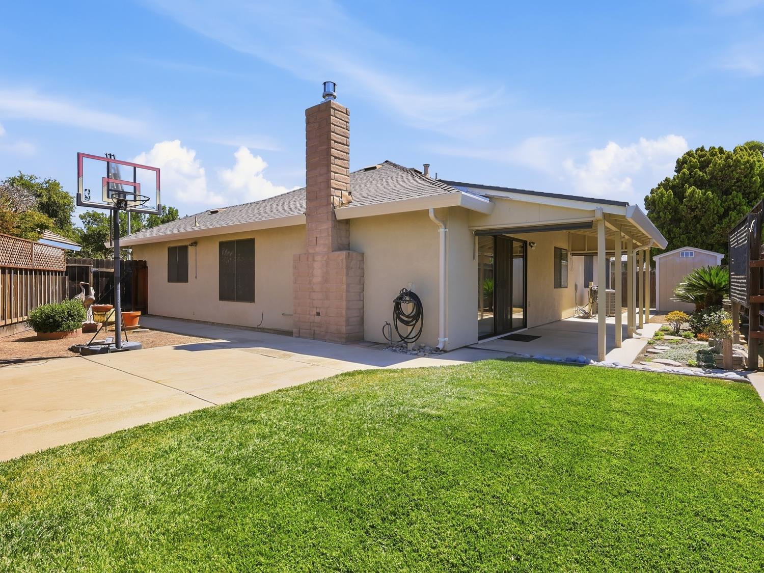 900 Multnomah Drive Modesto, CA 95350 - Photo 28 of 34 Expansive backyard featuring a lush lawn, concrete patio, covered patio structure, and a brick chimney