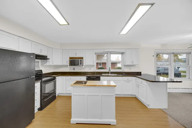 a kitchen with stainless steel appliances granite countertop a stove a sink dishwasher a refrigerator and white cabinets with wooden floor