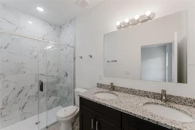 a bathroom with a granite countertop sink a toilet a mirror a bathtub and shower