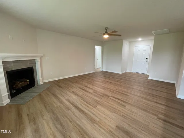 an empty room with wooden floor a chandelier fan and a fireplace