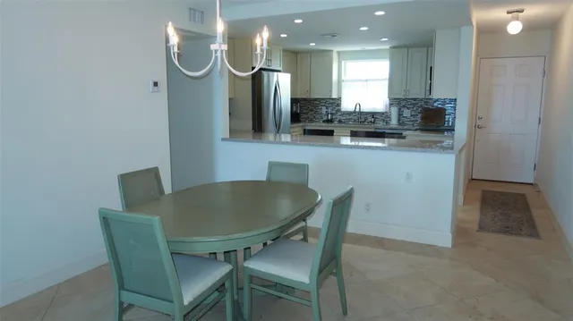 a kitchen with stainless steel appliances kitchen island granite countertop a dining table chairs and a refrigerator