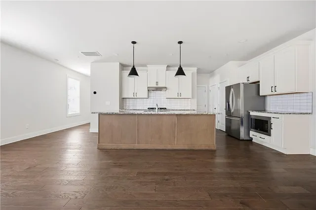 a large kitchen with stainless steel appliances kitchen island granite countertop a stove a sink a refrigerator and white cabinets with wooden floor