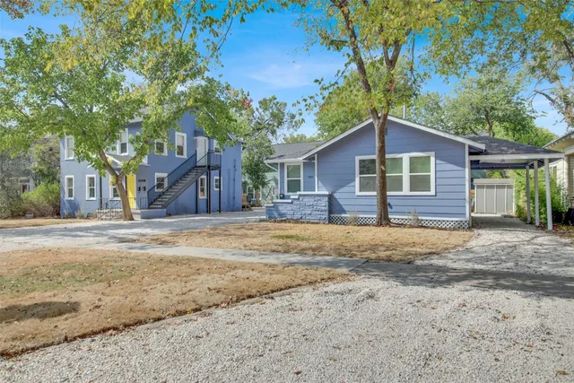 a front view of a house with a dirt yard and a large tree