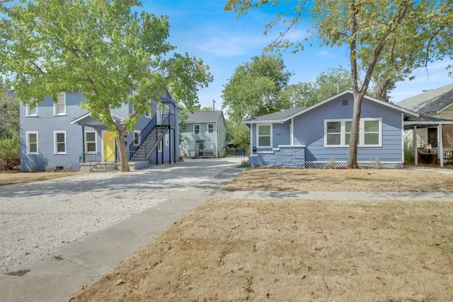 a front view of a house with a dirt yard and a large tree