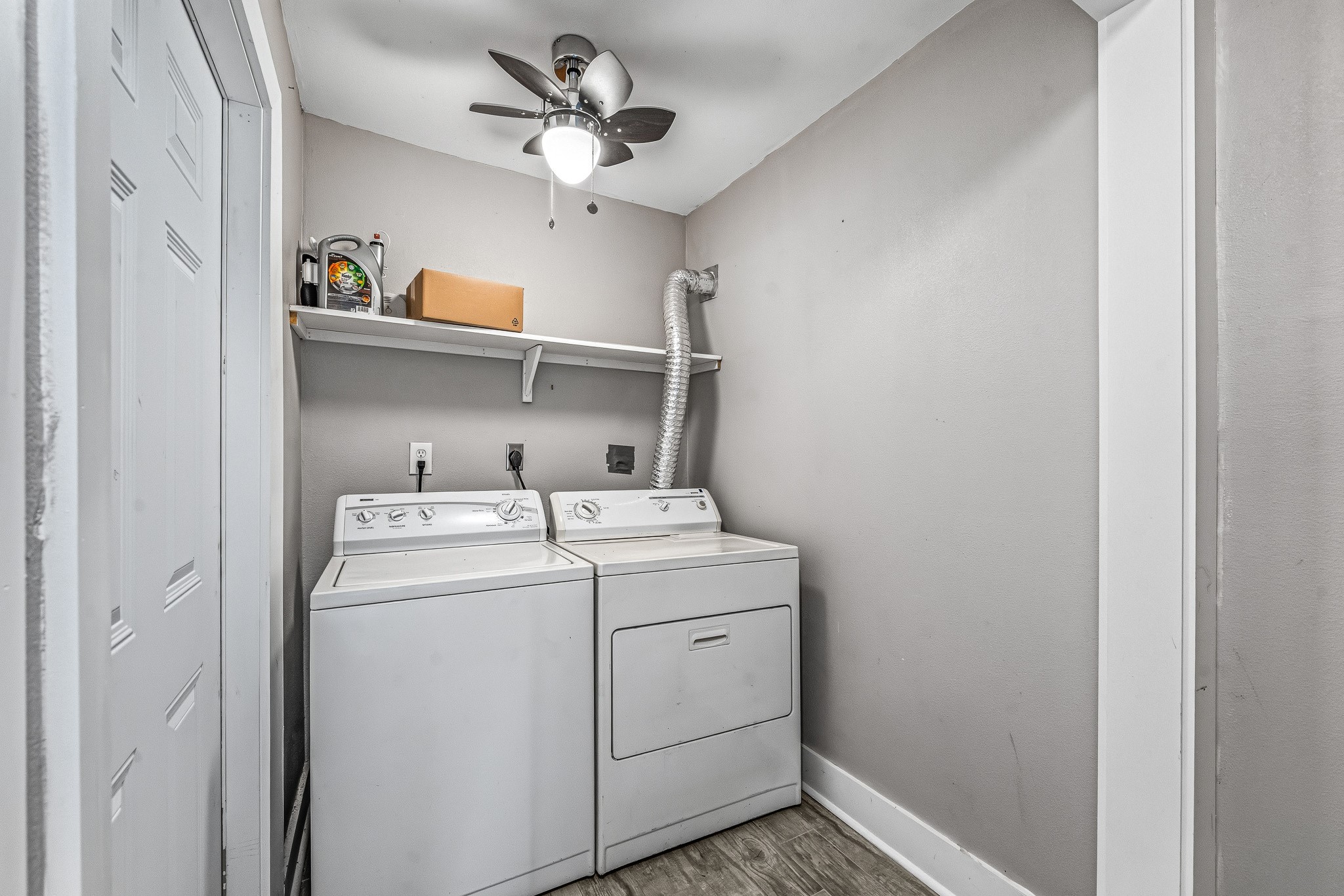 830 Threadneedle Street, Unit 240 Houston, TX 77079 - Photo 16 of 33 This photo shows a compact laundry room featuring a washer and dryer under a mounted shelf. The space has neutral walls, a ceiling fan with light, and wood-style flooring, providing a functional and efficient area for laundry tasks.
