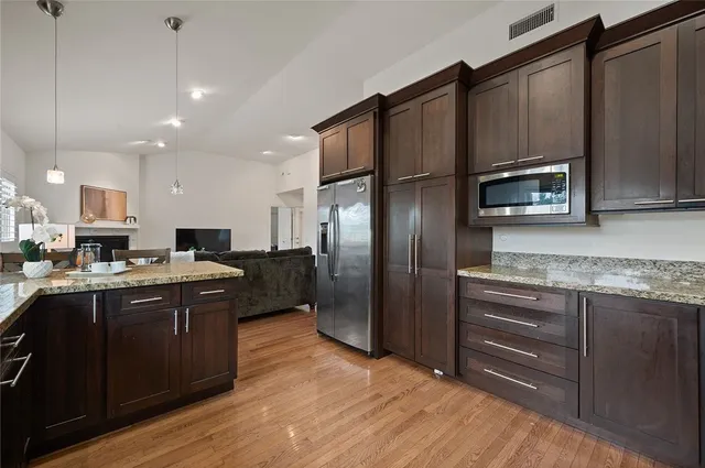 a kitchen with stainless steel appliances granite countertop a refrigerator a stove a sink dishwasher and wooden cabinets with wooden floor