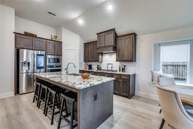 a kitchen with stainless steel appliances granite countertop a table chairs sink refrigerator and cabinets