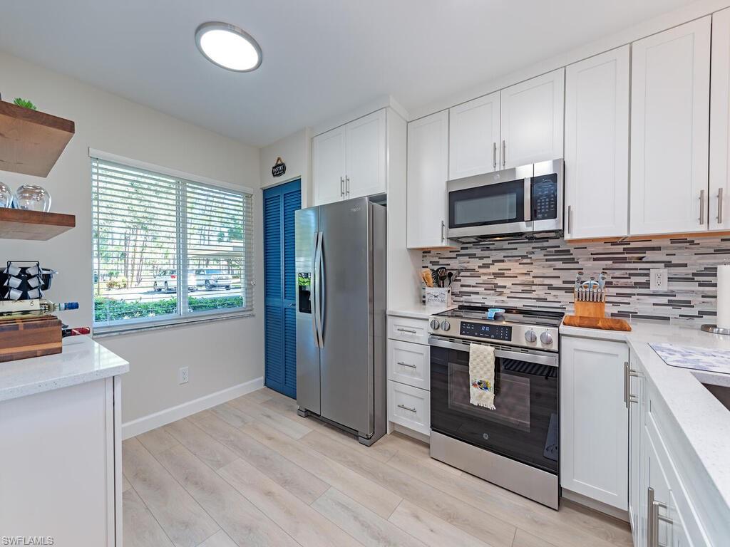 a kitchen with stainless steel appliances a stove a sink a refrigerator white cabinets and a window