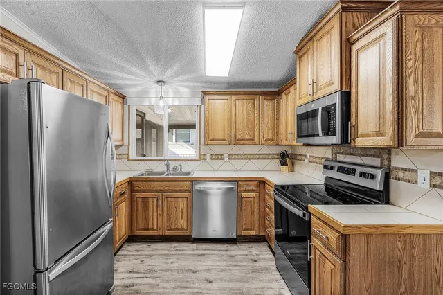 a kitchen with stainless steel appliances granite countertop a refrigerator a sink a stove top oven and a dishwasher with wooden floor