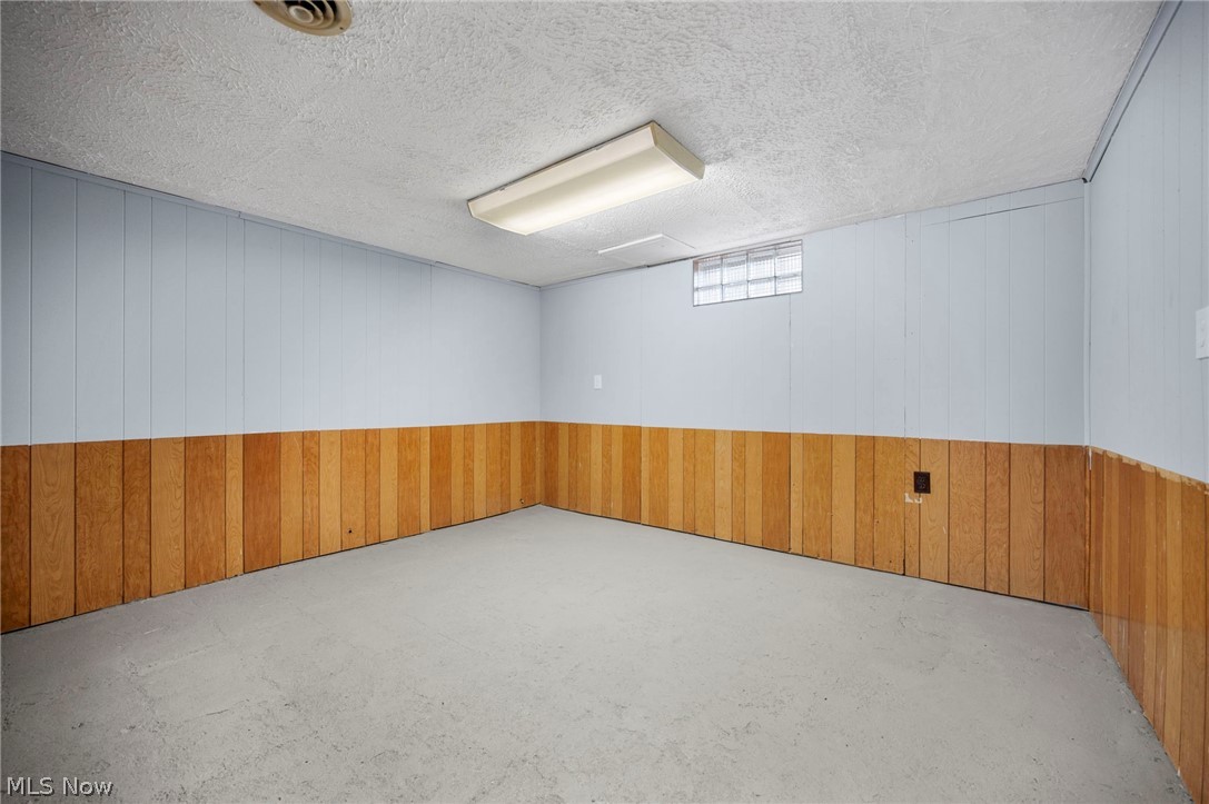 2099 Pontius Road Mogadore, OH 44260 - Photo 22 of 35 Empty rec room with wooden walls, a textured ceiling, and concrete floors