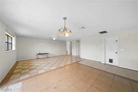 a view of an empty room with chandelier and wooden floor