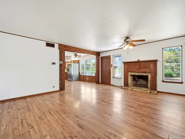 a view of an empty room with wooden floor fireplace and a window