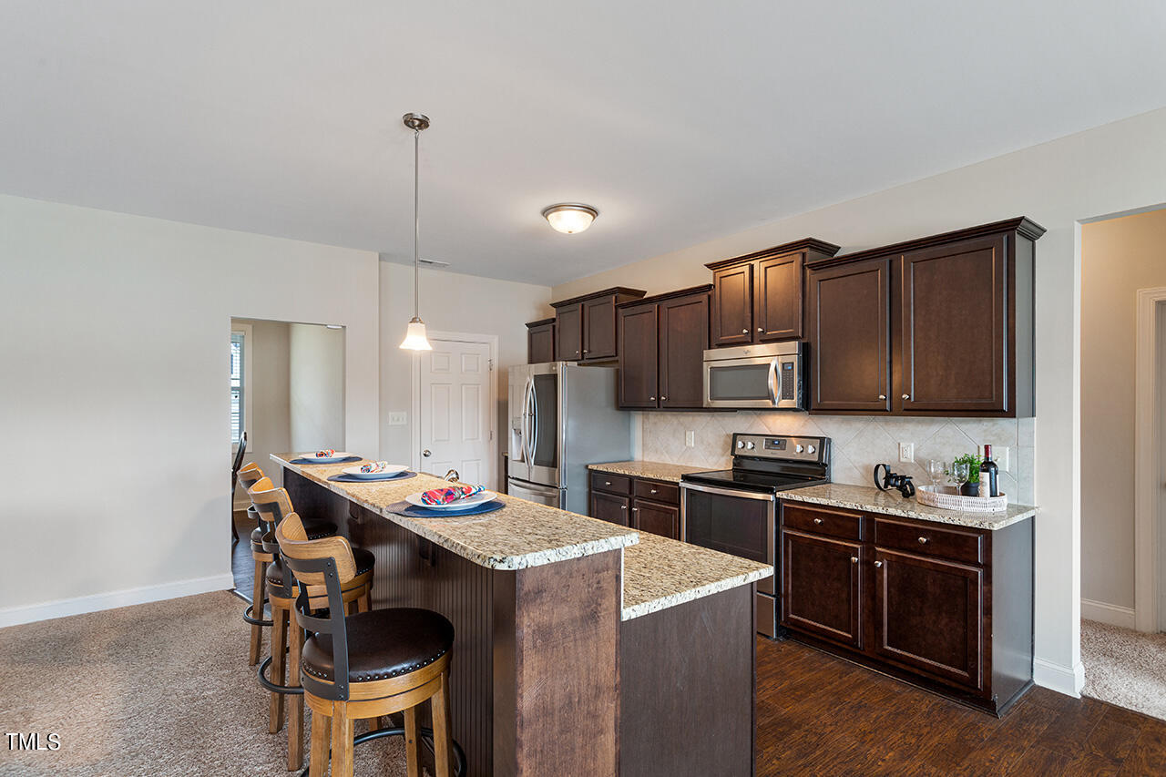 116 Celestial Drive Garner, NC 27529 - Photo 8 of 23 a kitchen with a stove a sink a kitchen island with chairs and wooden cabinets