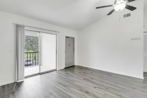 an empty room with wooden floor fan and windows