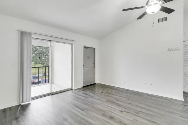 an empty room with wooden floor fan and windows