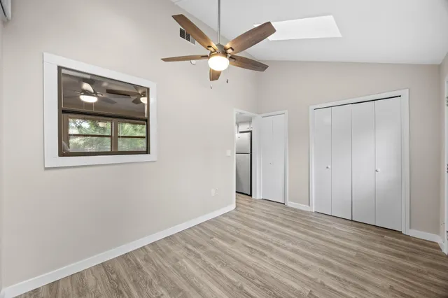 a view of an empty room with wooden floor and a ceiling fan
