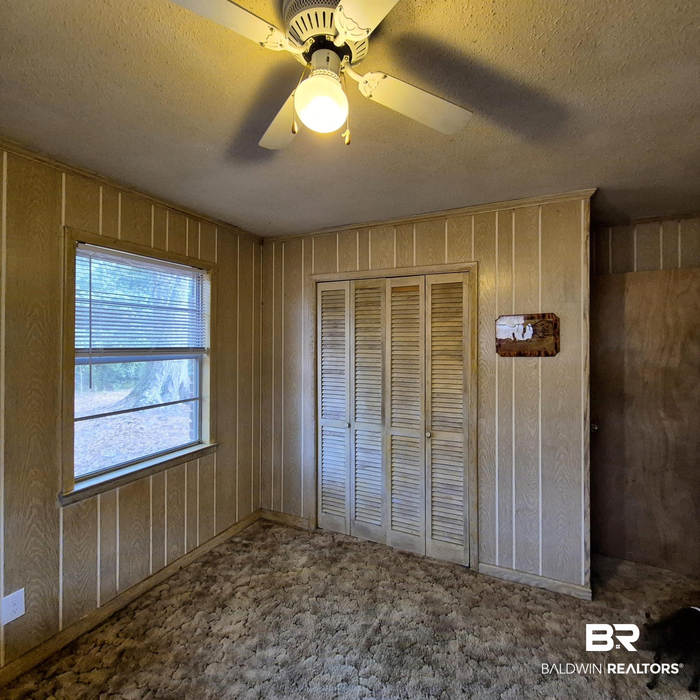 491 Forrest Avenue Castleberry, AL 36432 - Photo 16 of 33 Unfurnished bedroom featuring a textured ceiling, ceiling fan, a closet, and wood walls