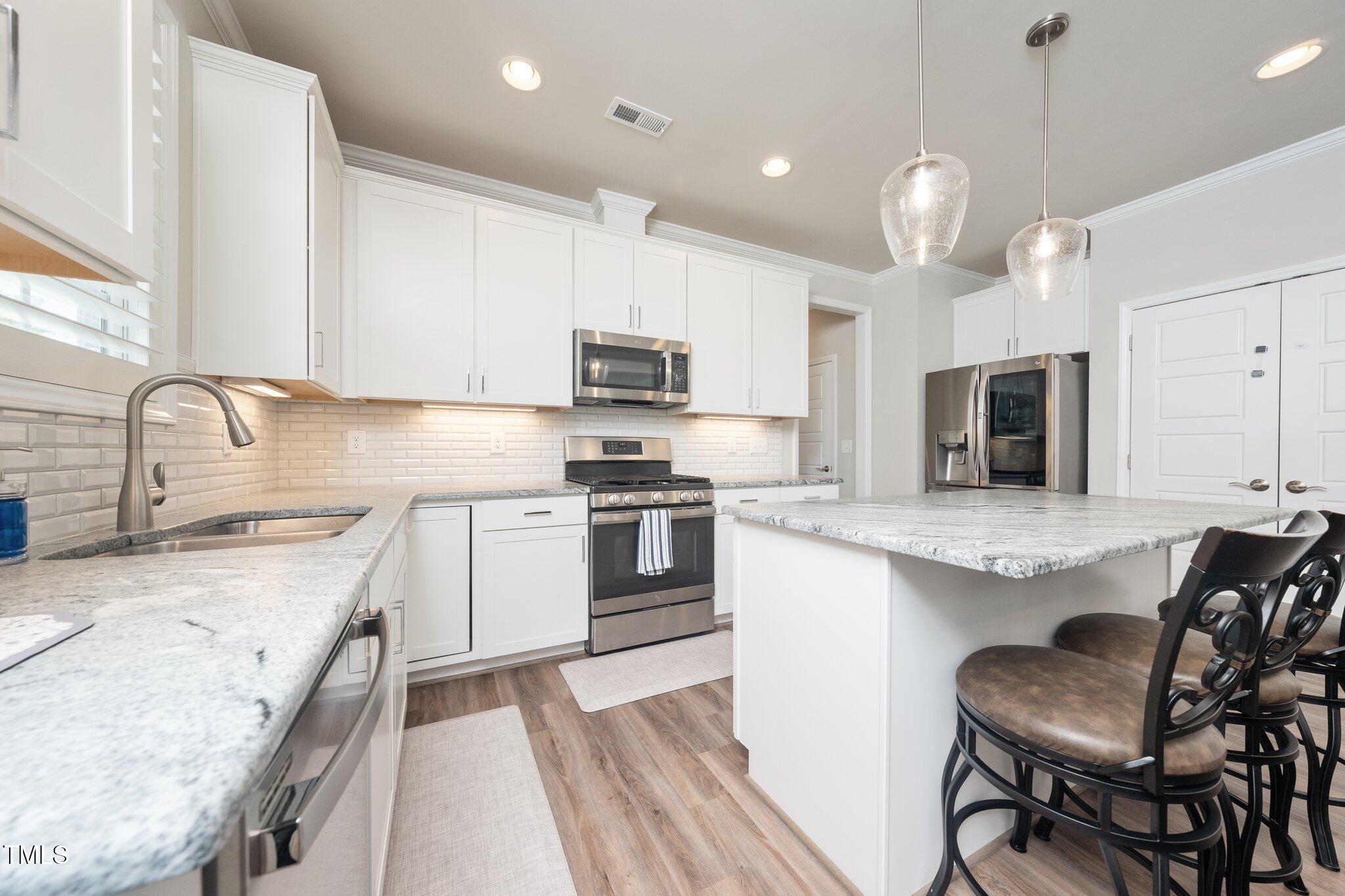 1705 Main Divide Drive Wake Forest, NC 27587 - Photo 6 of 47 a kitchen with stainless steel appliances granite countertop a stove top oven a sink dishwasher a dining table and chairs with wooden floor