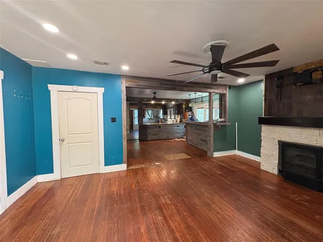 a view of a livingroom with a fireplace a ceiling fan and wooden floor