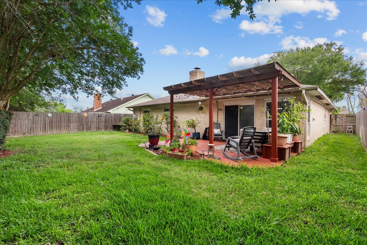 883 Silverpines Road Houston, TX 77062 - Photo 38 of 38 This photo showcases a spacious backyard with a lush green lawn and a charming patio area. The patio features a pergola and seating, perfect for outdoor relaxation. The yard is fenced, providing privacy and a cozy atmosphere.