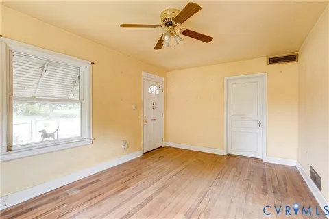 an empty room with wooden floor fan and windows