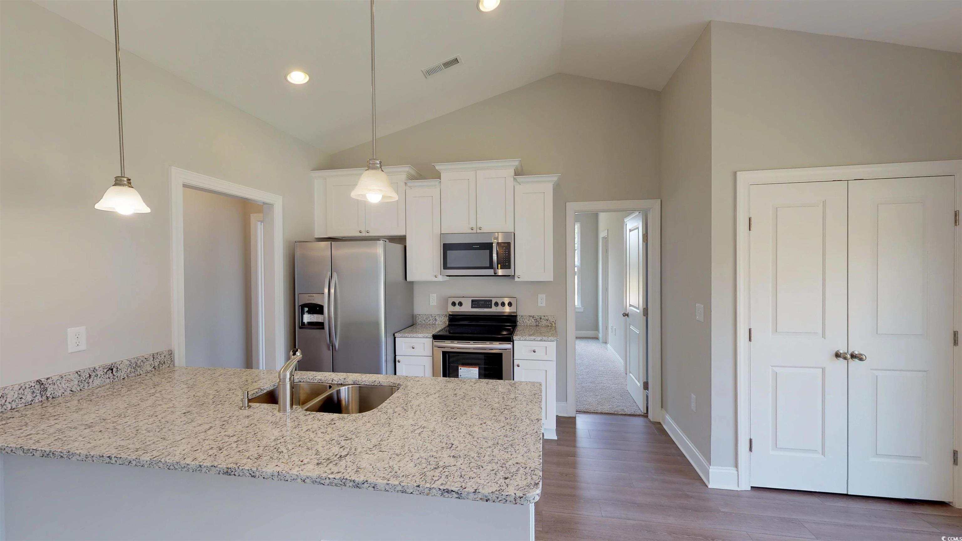29 Wimbledon Court, Unit WVC 8 Pawleys Island, SC 29585 - Photo 4 of 12 Kitchen featuring appliances with stainless steel finishes, white cabinets, light stone counters, a peninsula, and vaulted ceiling