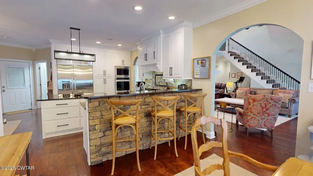 a kitchen with stainless steel appliances kitchen island granite countertop a stove a refrigerator and white cabinets with wooden floor