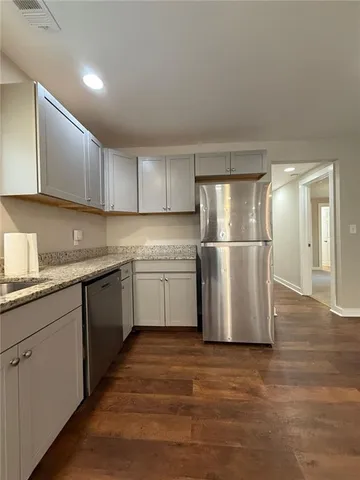 a view of an empty room with wooden floor and a kitchen