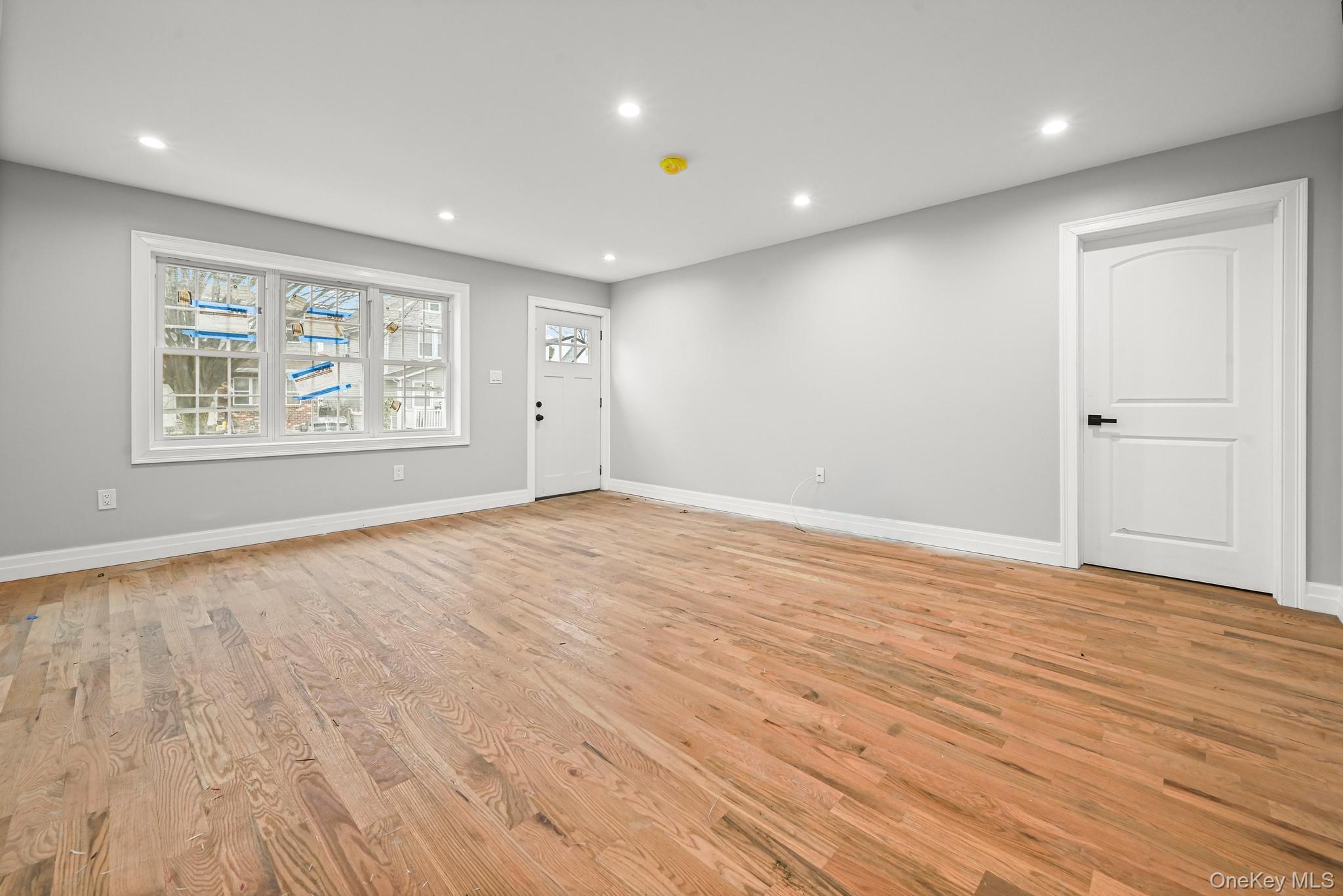 160-15 118th Road Queens, NY 11434 - Photo 4 of 23 an empty room with wooden floor and windows