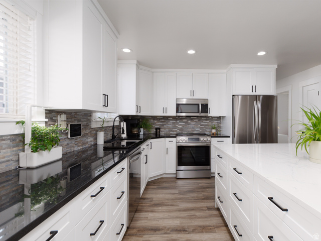8252 Wood Street Midvale, UT 84047 - Photo 3 of 40 Modern kitchen featuring white cabinetry with black hardware, dark granite countertops, a mosaic tile backsplash, stainless steel appliances, and wood-finish flooring