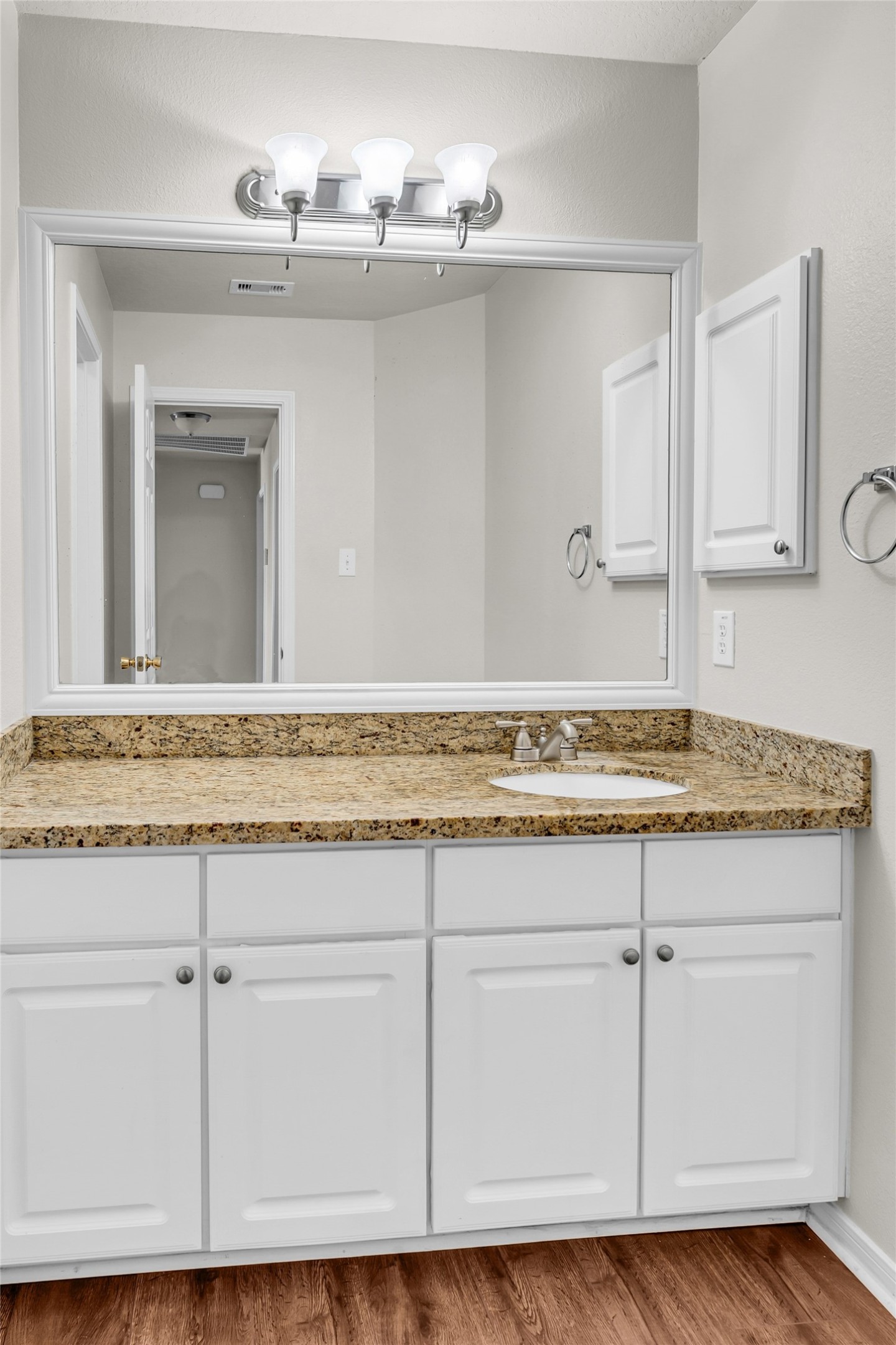 5018 Mabry Stream Court Katy, TX 77449 - Photo 18 of 31 This bathroom features a large mirror with overhead lighting, granite countertop, white cabinetry, and laminate flooring, offering a clean and modern look.