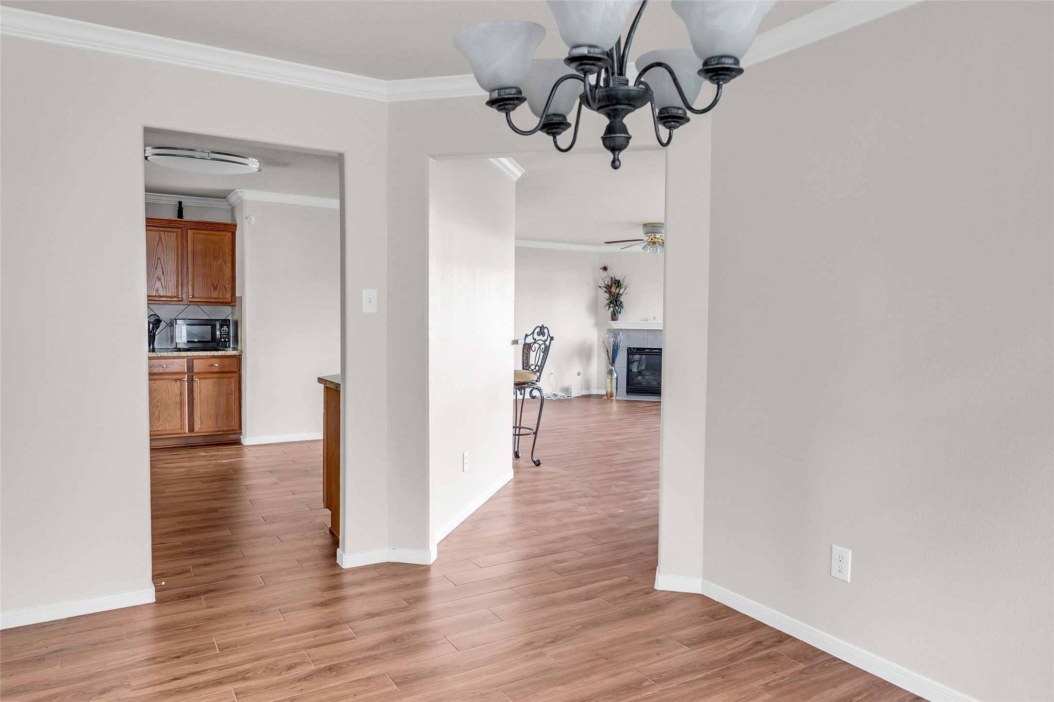 5018 Mabry Stream Court Katy, TX 77449 - Photo 4 of 31 This photo shows a bright, open space with light LVP flooring. There's a view into a kitchen with wooden cabinets and a microwave, and an adjacent living area with a ceiling fan and a fireplace. The room is well-lit with a decorative chandelier.