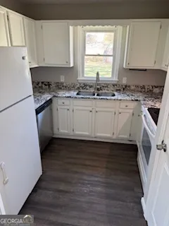 a kitchen with granite countertop white cabinets white appliances a sink and a hard wood floor