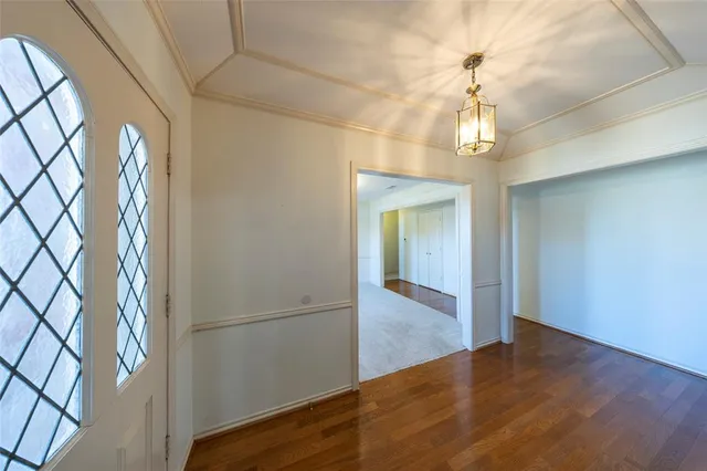 an empty room with wooden floor chandelier and entryway