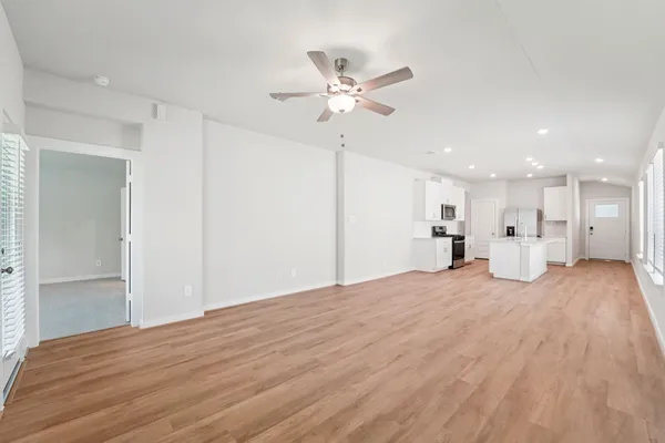 a view of a livingroom with a kitchen space with wooden floor and a ceiling fan