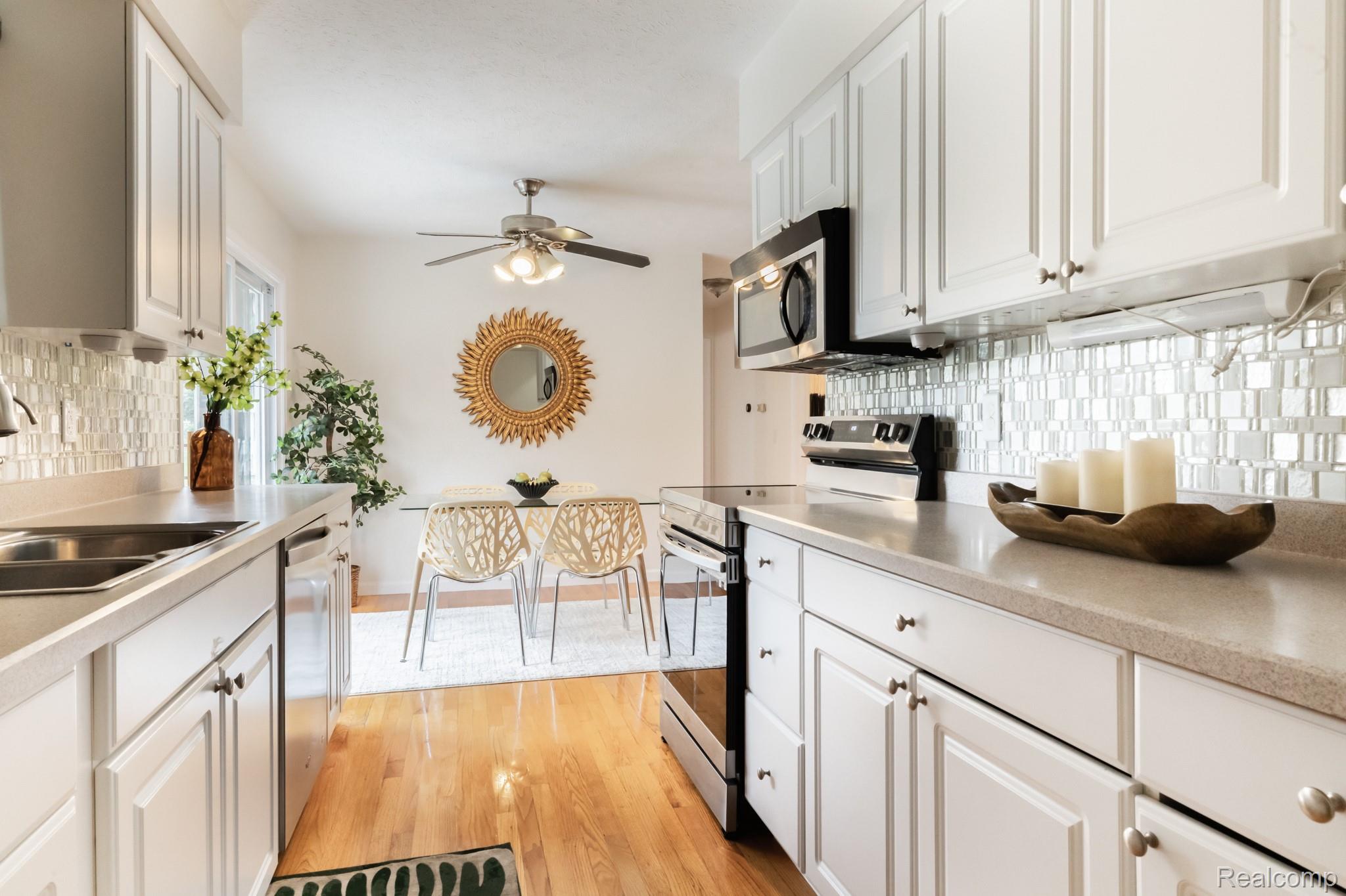 3882 Okemos Road Okemos, MI 48864 - Photo 19 of 50 Galley kitchen featuring white cabinetry with brushed metal hardware, white subway tile backsplash, stainless steel appliances, light wood-finish flooring, and quartz countertops