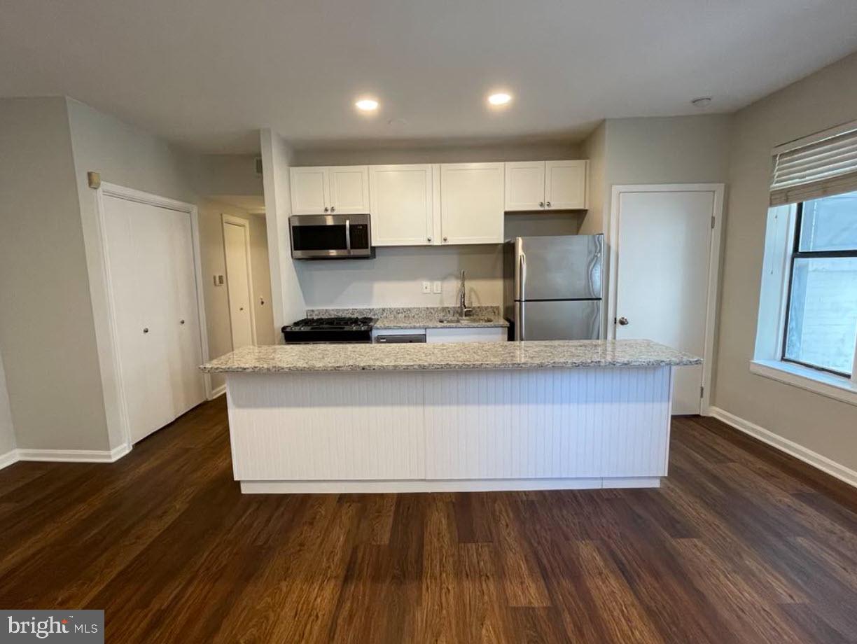 1669 Columbia Road Northwest, Unit 215 Washington, DC 20009 - Photo 14 of 25 a kitchen with kitchen island granite countertop wooden floors white cabinets and stainless steel appliances