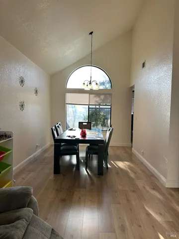 a room with stainless steel appliances kitchen island granite countertop a refrigerator a stove a sink a dining table and chairs with wooden floor