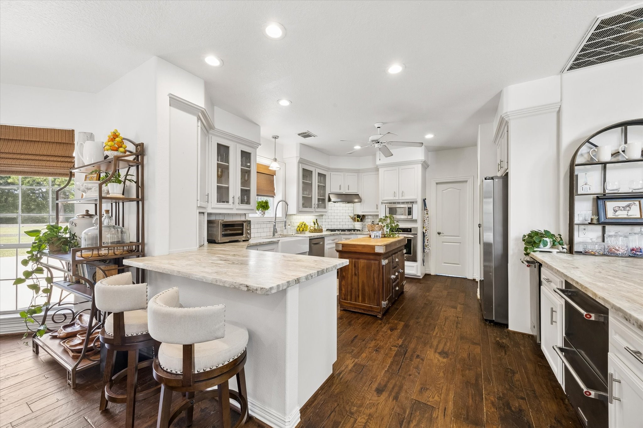 6819 Still Meadow Street Spring, TX 77389 - Photo 19 of 50 Bright, spacious kitchen with elegant white cabinetry, a central island, and granite countertops, complemented by rich wood flooring and modern stainless steel appliances.