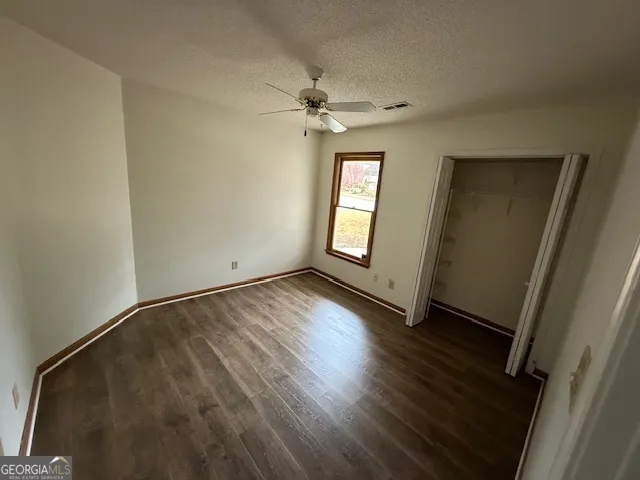 an empty room with wooden floor fan and windows