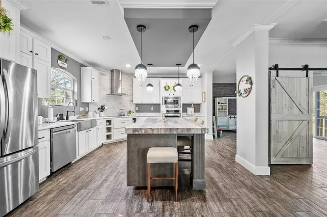 a kitchen with granite countertop a refrigerator a sink dishwasher a stove and white cabinets with wooden floor