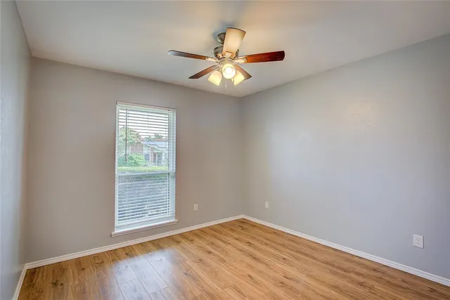 an empty room with wooden floor fan and windows