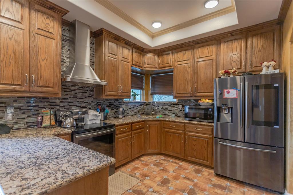 8900 Holly Road Alvarado, TX 76009 - Photo 8 of 17 Kitchen featuring wood cabinetry, stainless steel appliances, mosaic tile backsplash, stone countertops, and a tray ceiling with recessed lighting
