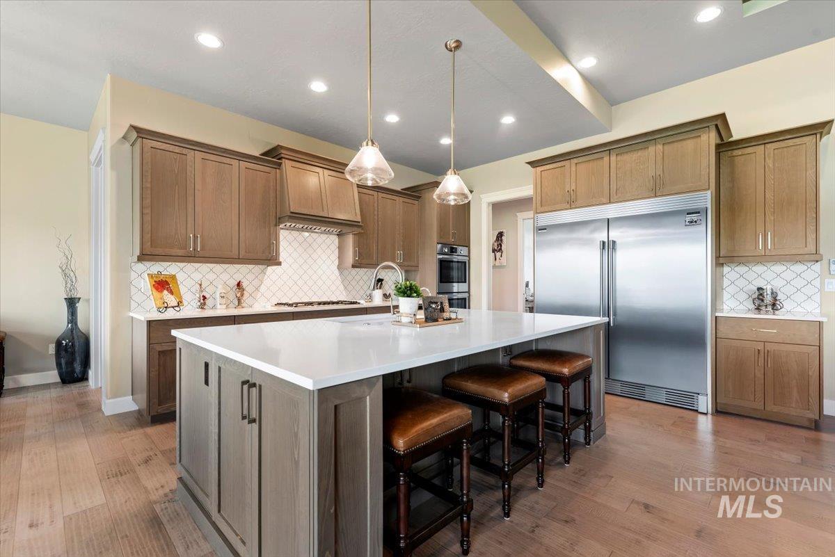 15465 Syrah Court Caldwell, ID 83607 - Photo 13 of 45 Kitchen featuring appliances with stainless steel finishes, backsplash, wood finished floors, an island with sink, and light countertops