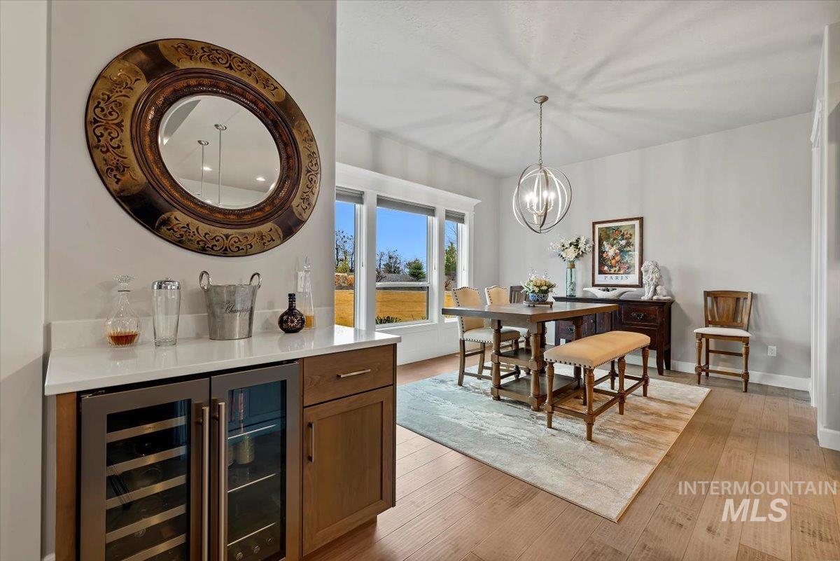 15465 Syrah Court Caldwell, ID 83607 - Photo 14 of 50 Bar area featuring wine cooler, light wood-type flooring, wood finish cabinets, a chandelier, and light stone countertops